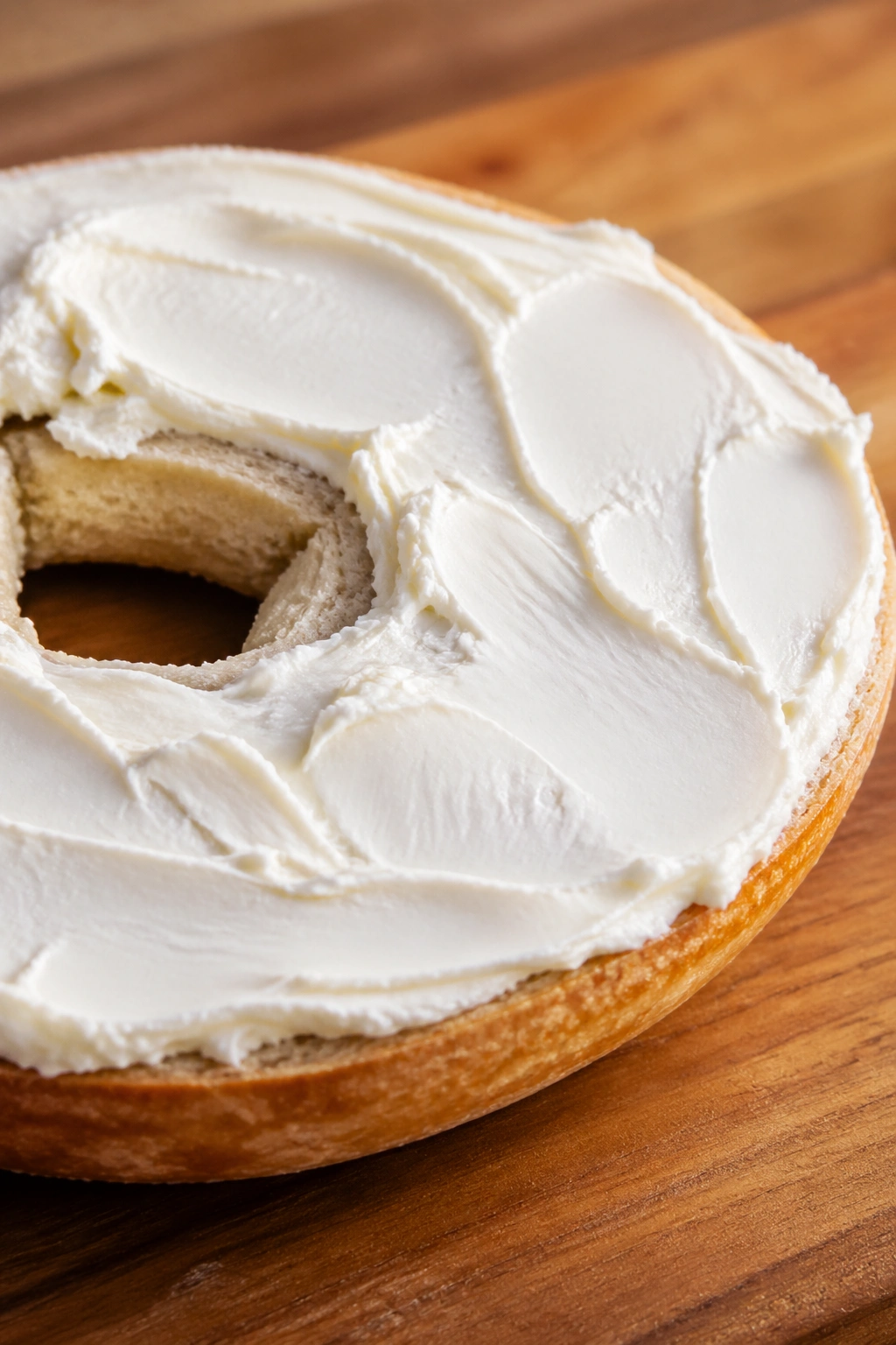 Close-up of half a plain bagel with cream cheese on a wooden board