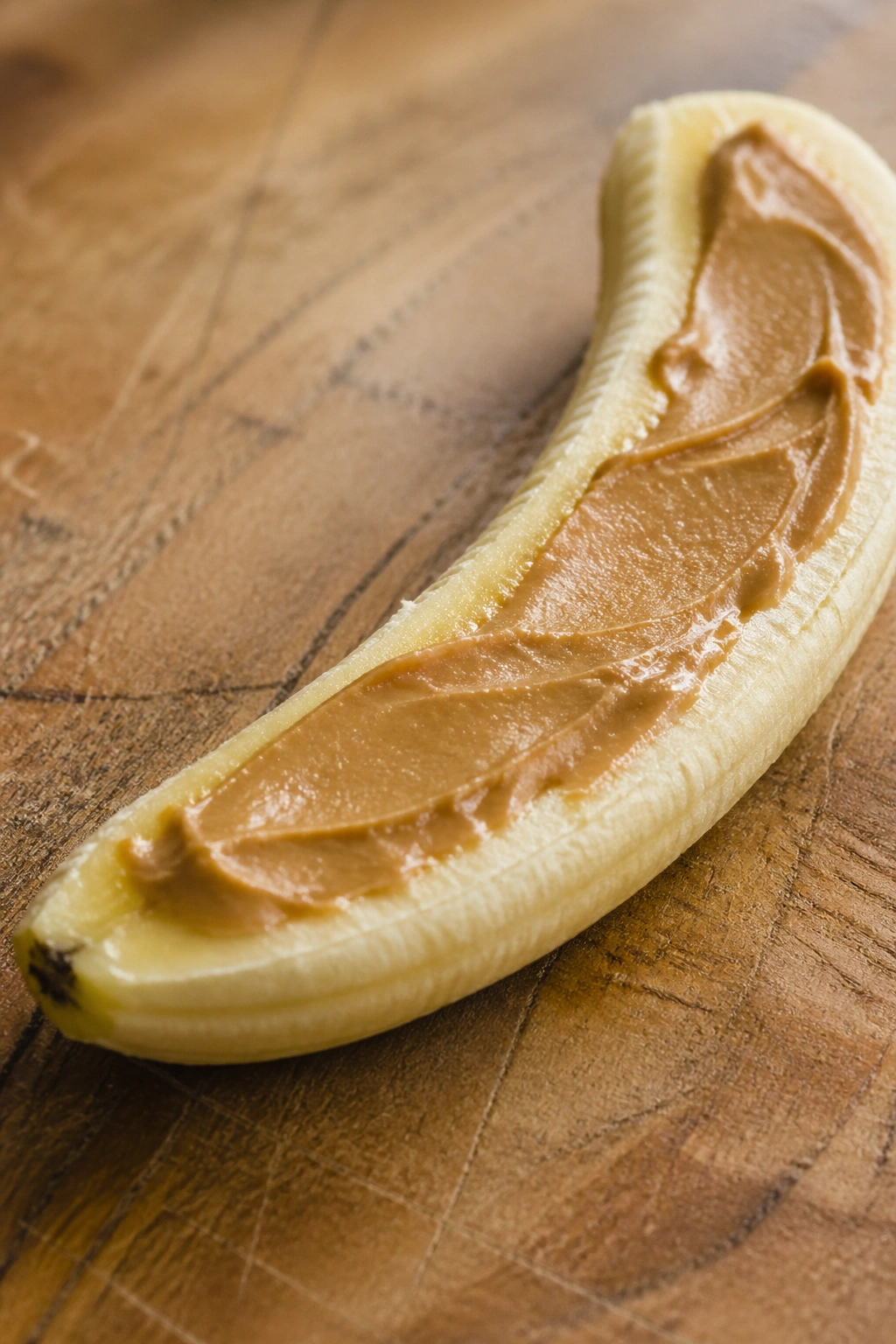 Close-up of a banana with peanut butter on a wooden cutting board, ready-to-eat pre-workout snack.
