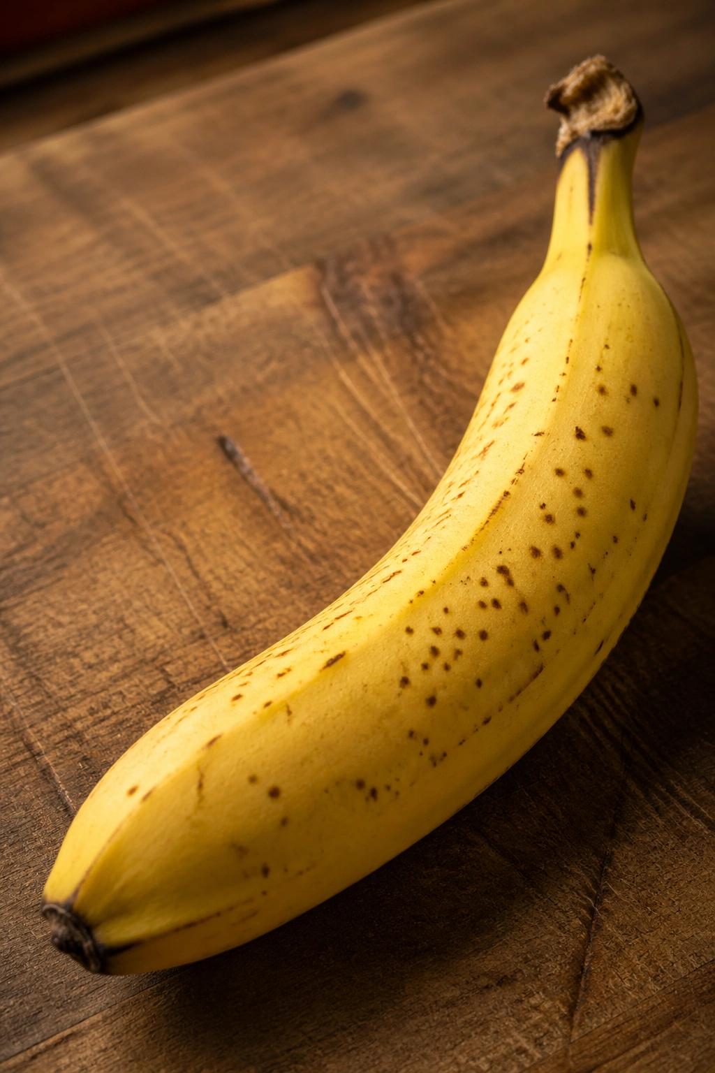 Close-up of a single ripe banana on a wooden cutting board in a warm kitchen