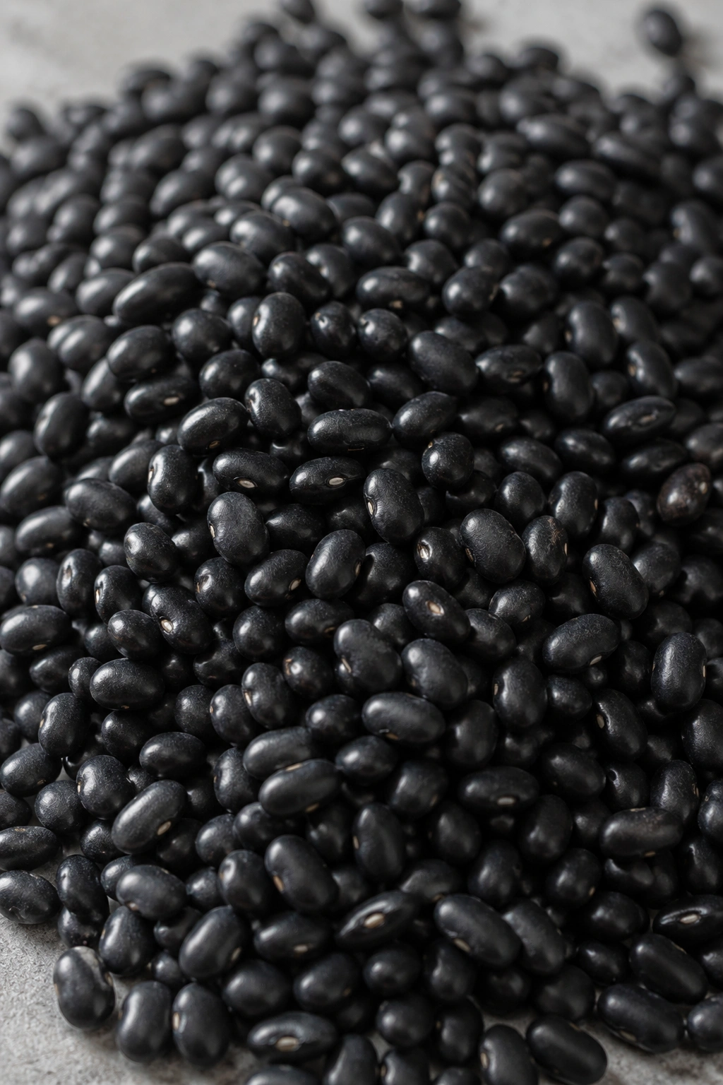 Close-up of glossy black beans filling the frame on a neutral surface