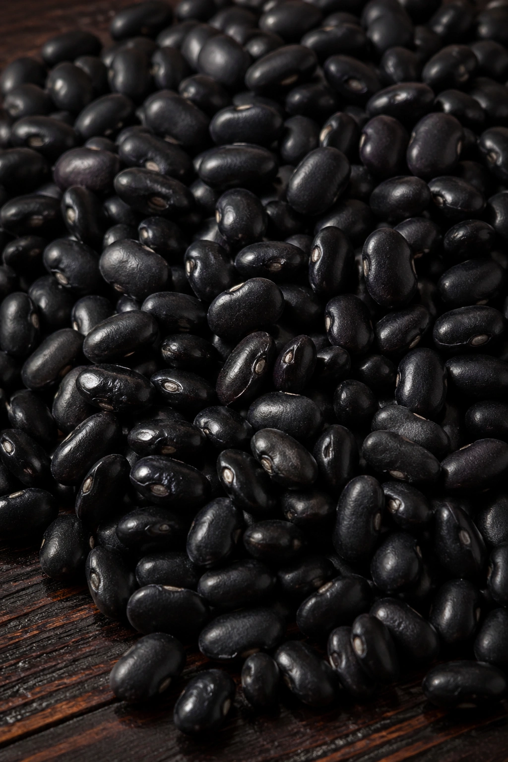 Close-up of glossy black beans on a dark wooden surface