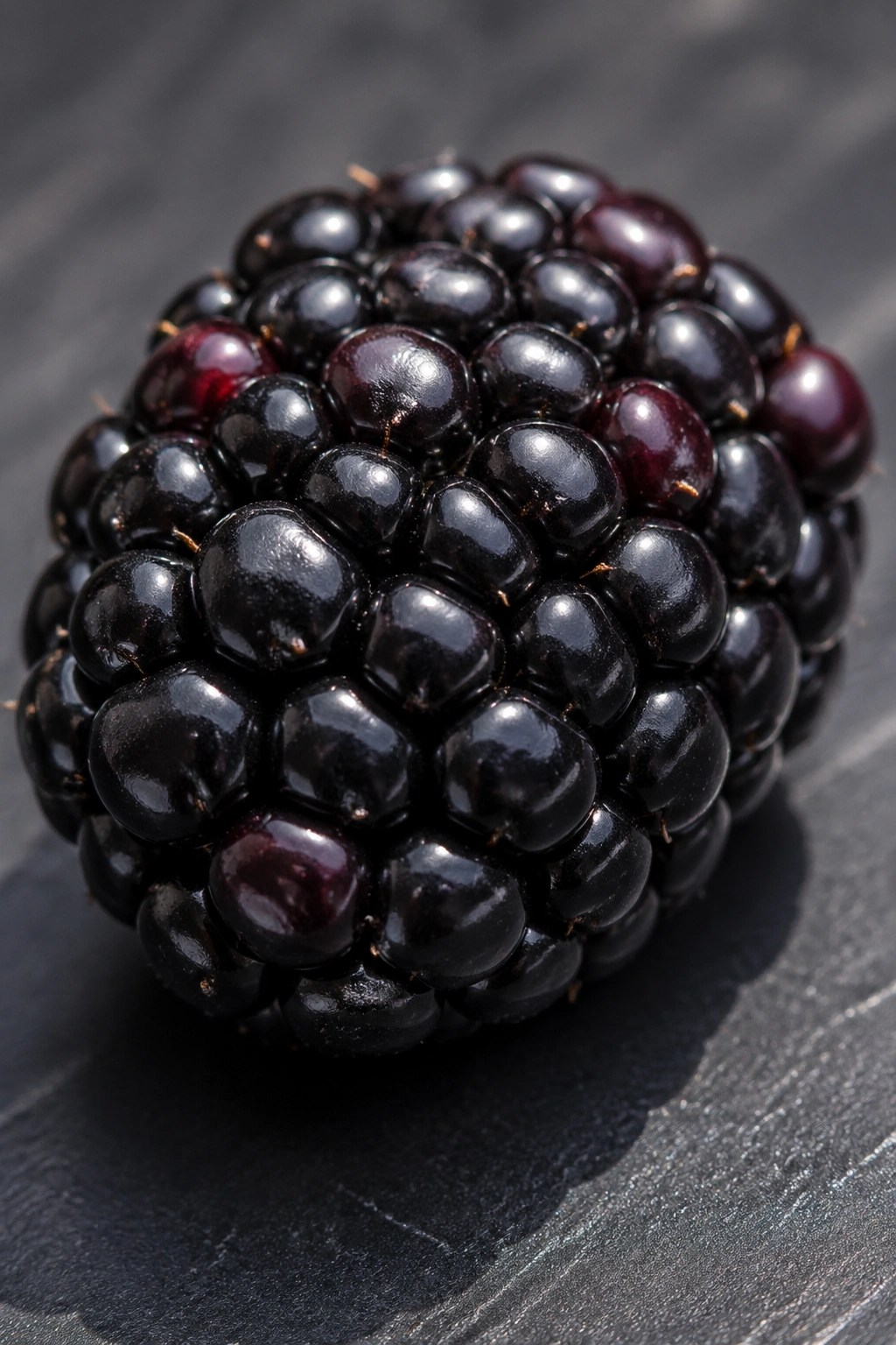 Close-up of a single blackberry on a slate surface