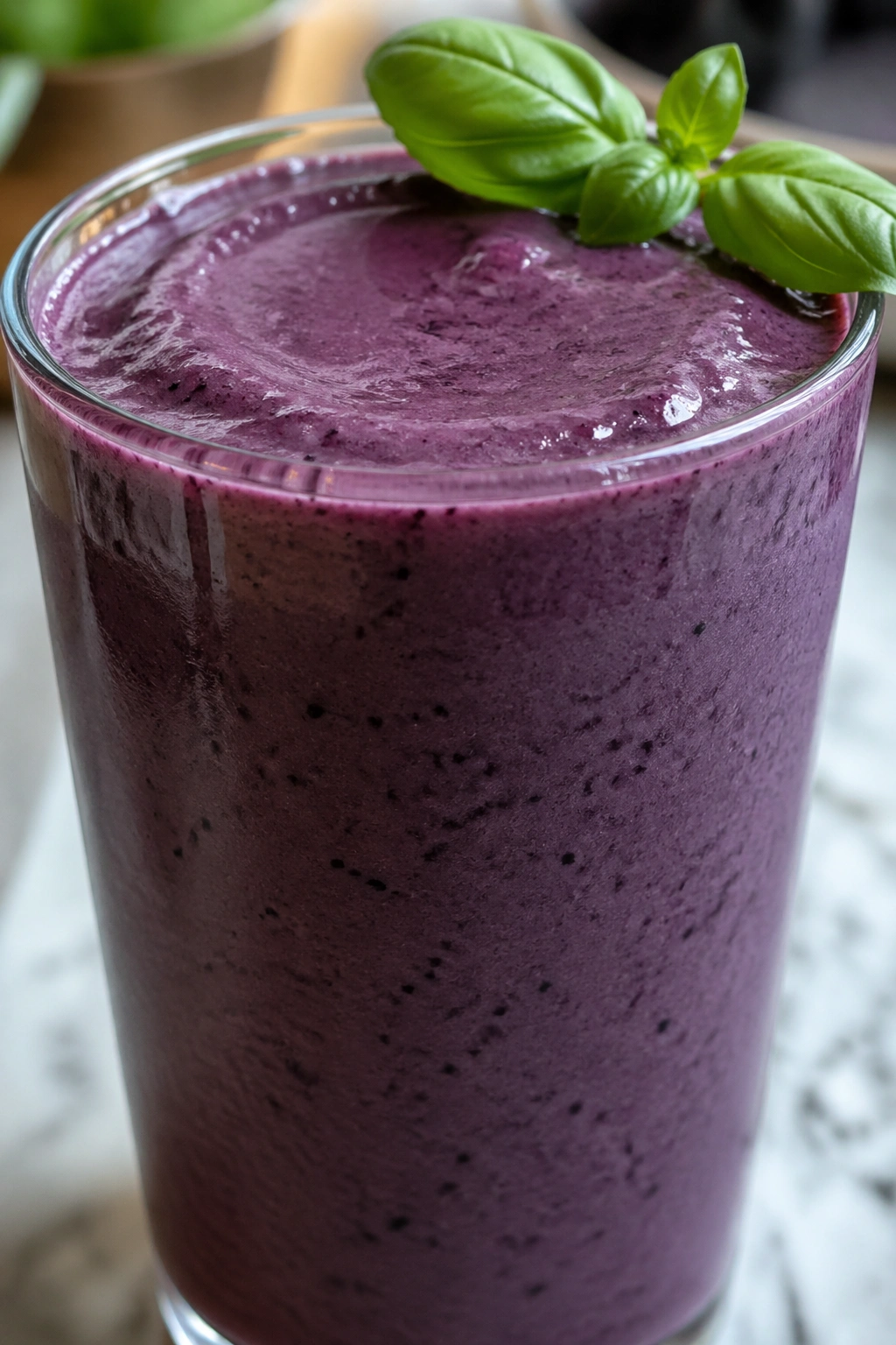Deep purple blueberry basil smoothie in a glass with basil leaves at the rim.