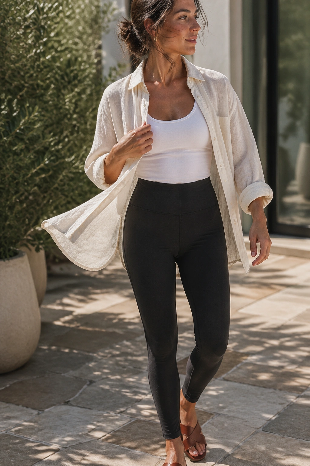 Close-up of a real person wearing a linen shirt over a tank with yoga pants and sandals outdoors in warm sunlight