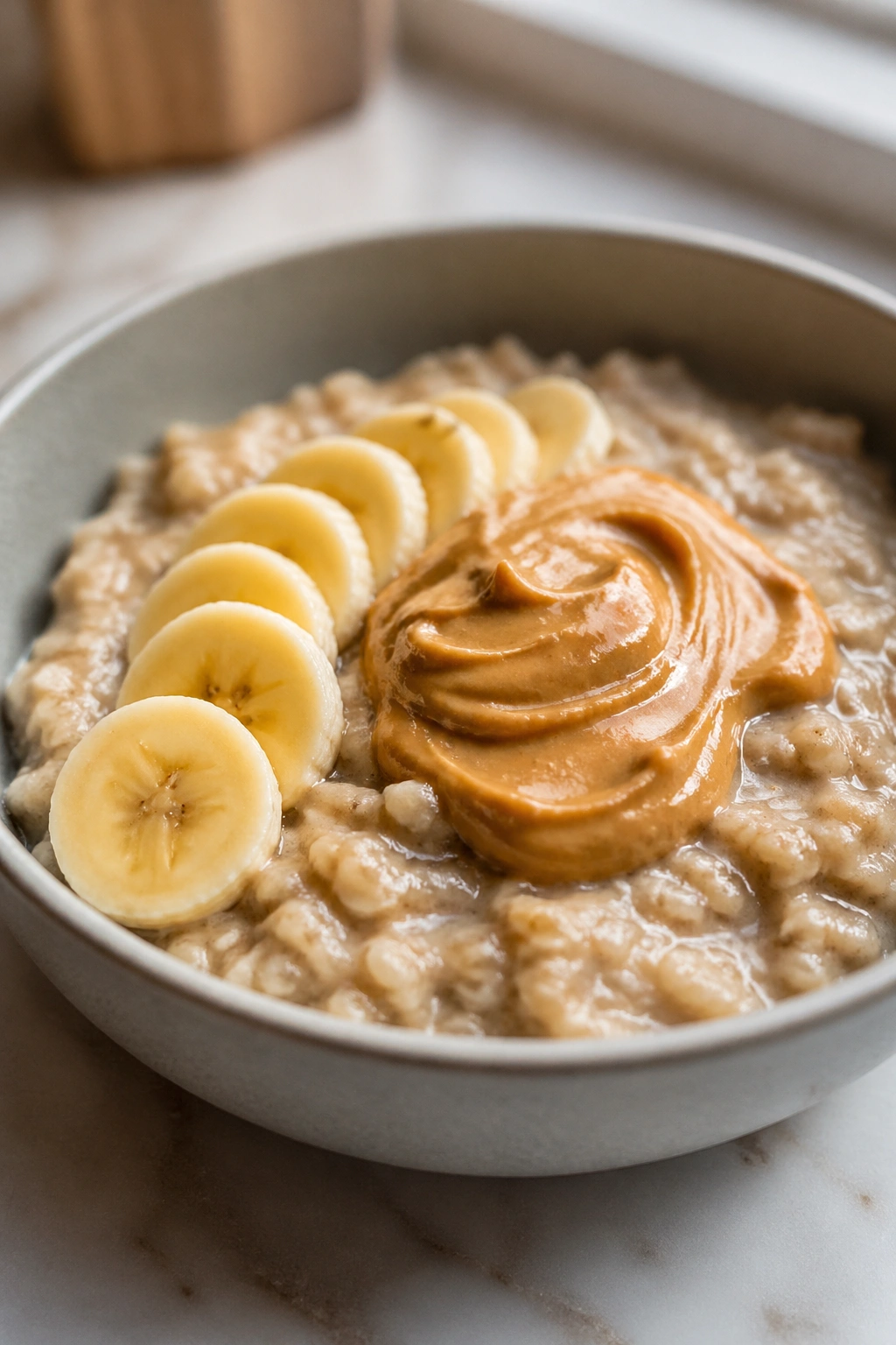 Close-up of protein oatmeal with banana slices and peanut butter on a breakfast counter