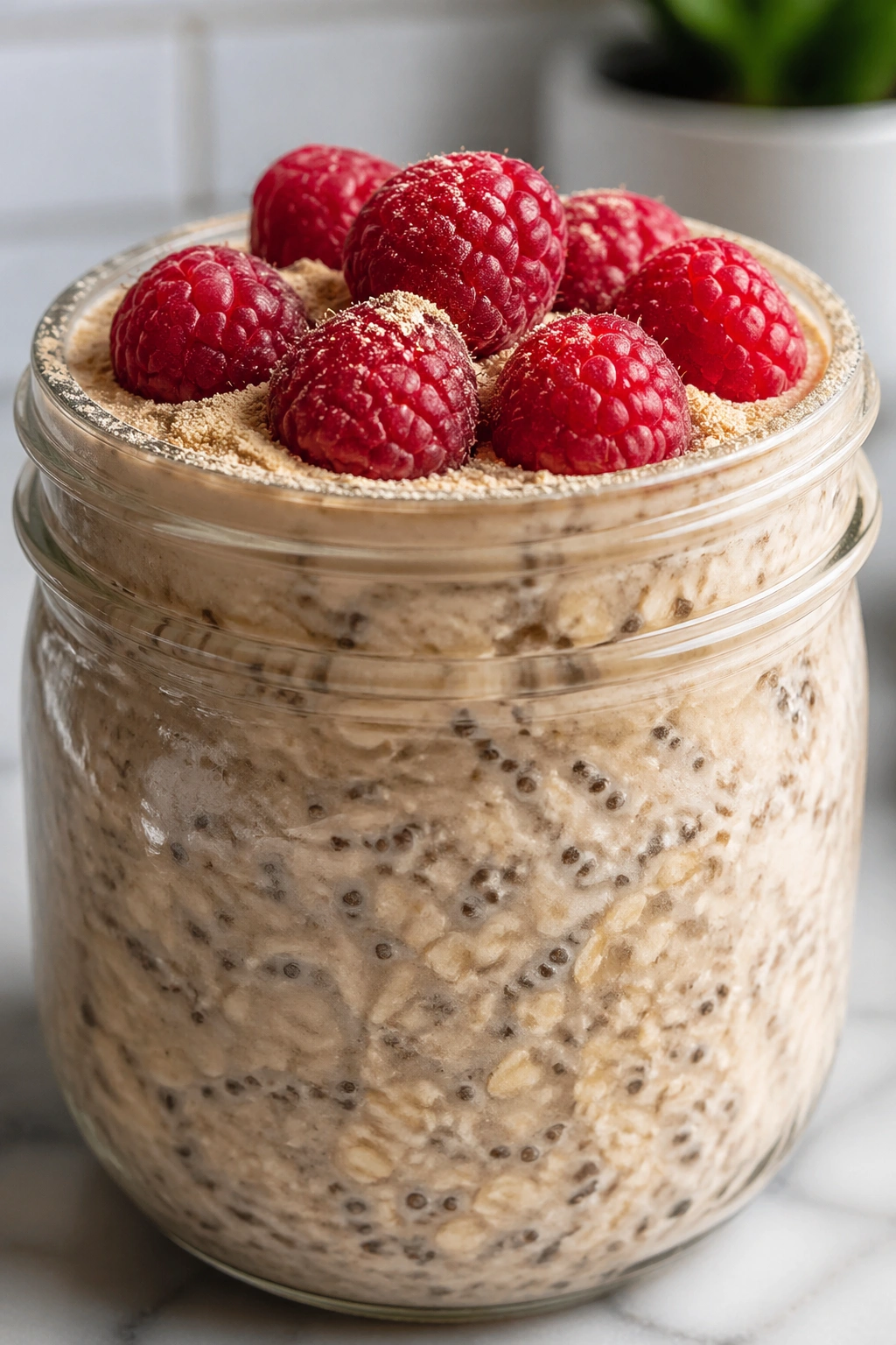 Close-up of overnight oats with raspberries in a glass jar on a kitchen counter