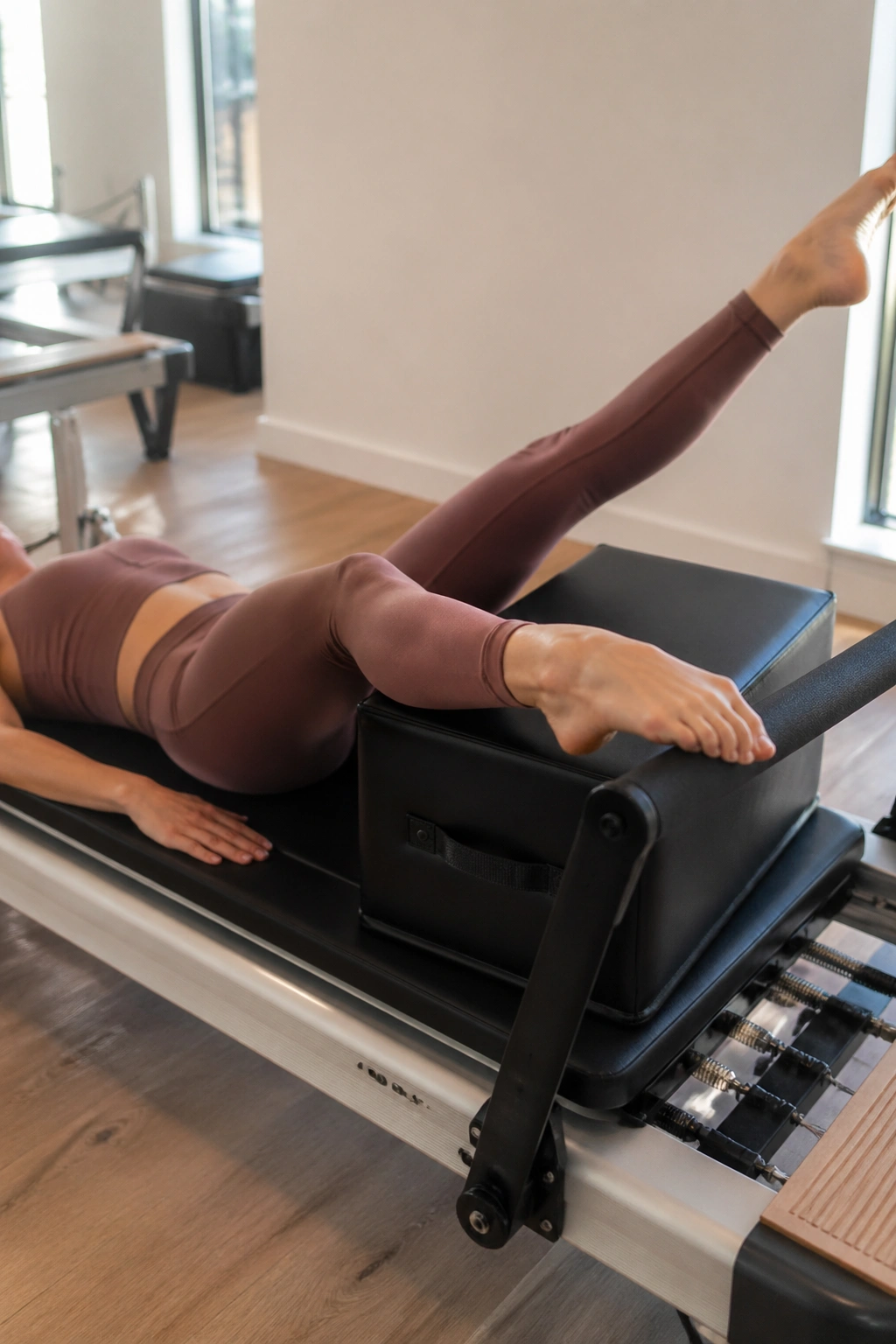 Close-up of a person performing reformer footwork on a Pilates reformer with a long box in a bright studio