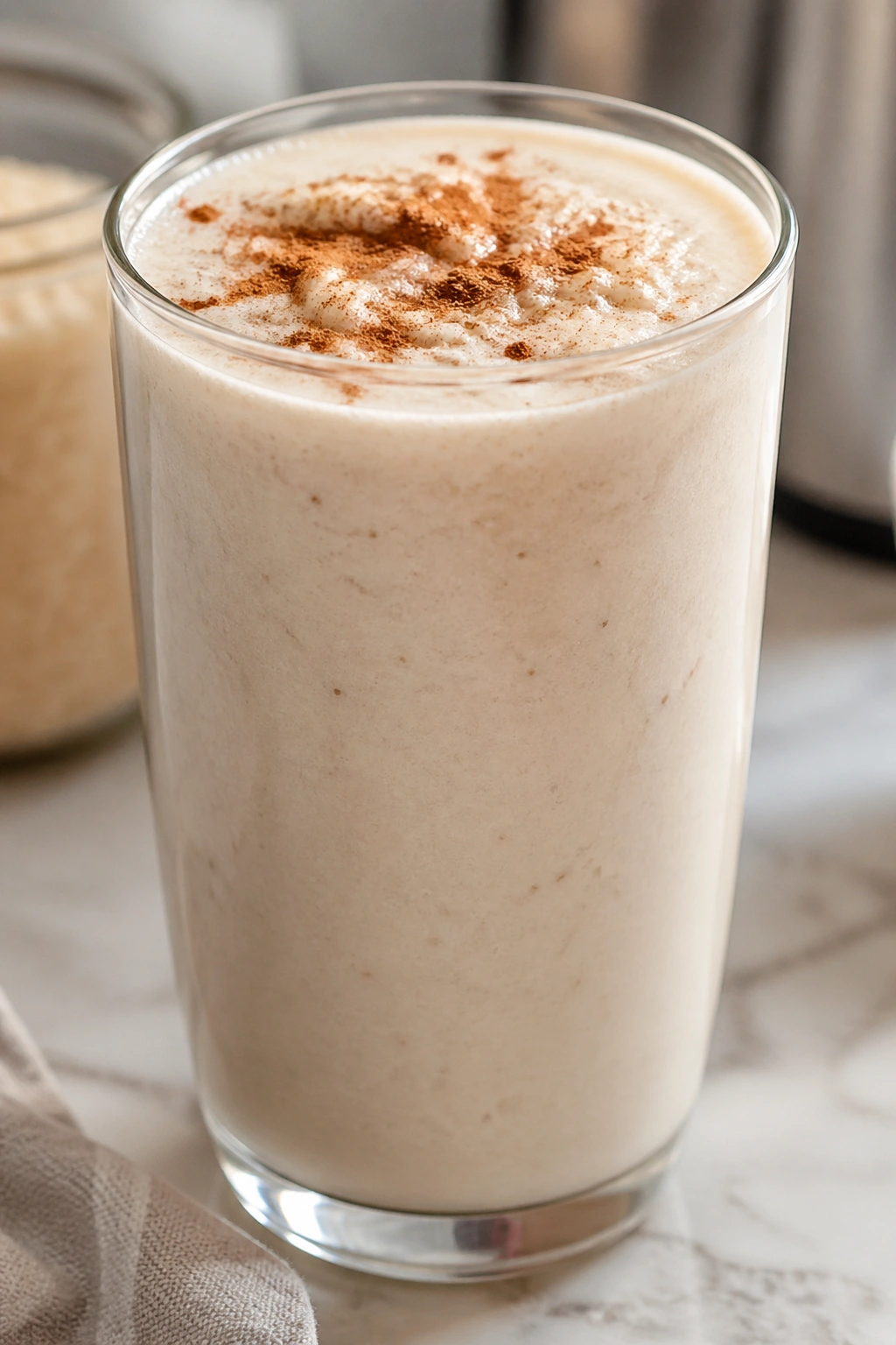 Creamy rice pudding recovery smoothie in a glass with cinnamon dust on top on a kitchen counter