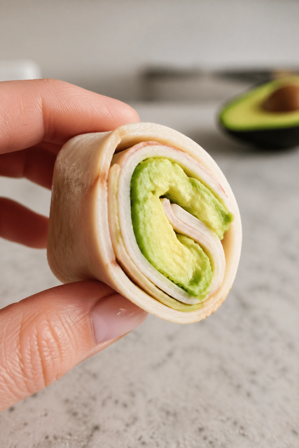 Close-up of a turkey and avocado roll-up held in hand
