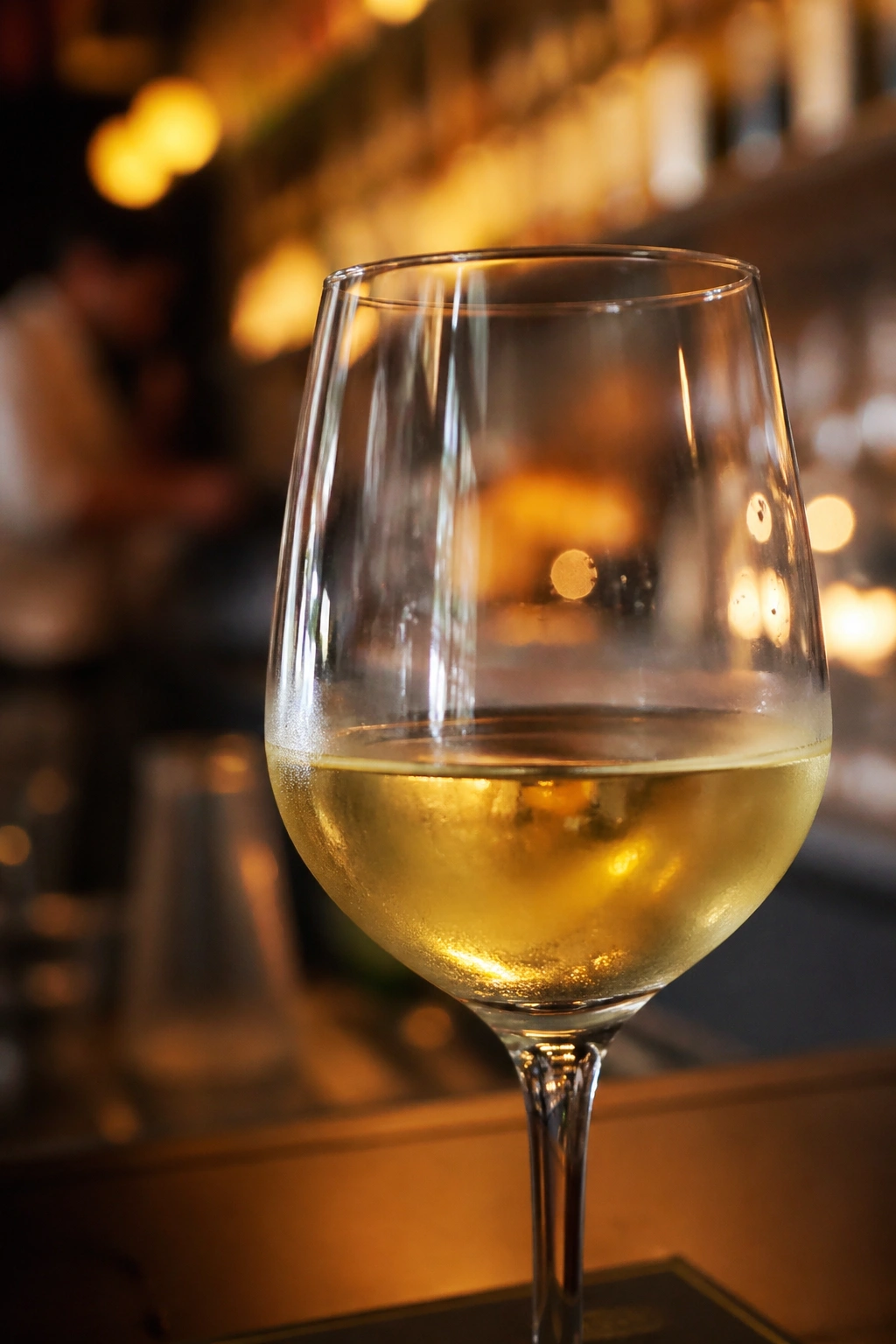 Close-up of a glass of white wine filling the frame with warm bar lighting