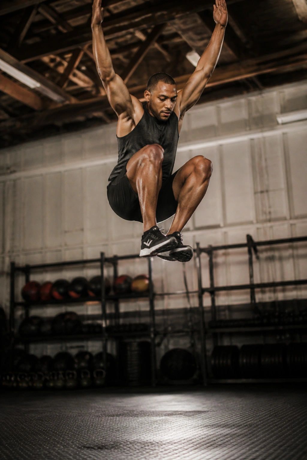 Athlete performing burpees with tuck jump mid-air, gym setting.