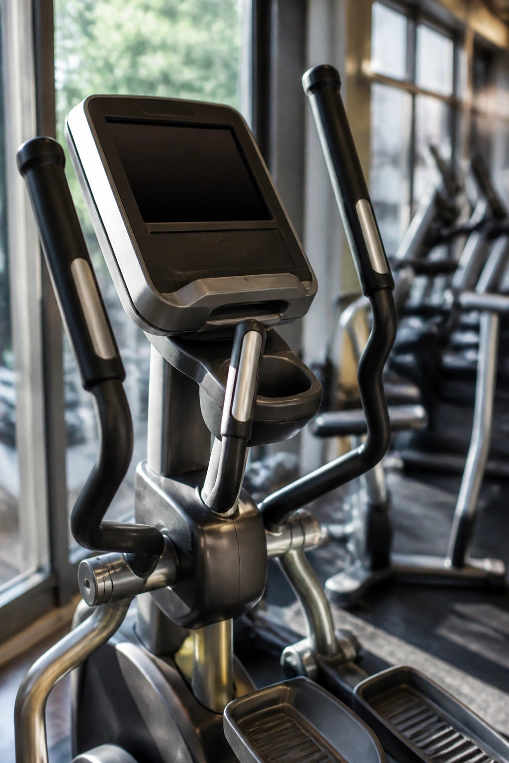 Close-up of elliptical trainer console and moving handles in a modern gym.
