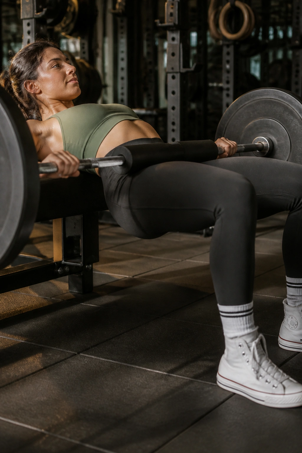 Athlete performing hip thrust with barbell on hips atop a bench; glutes contracted