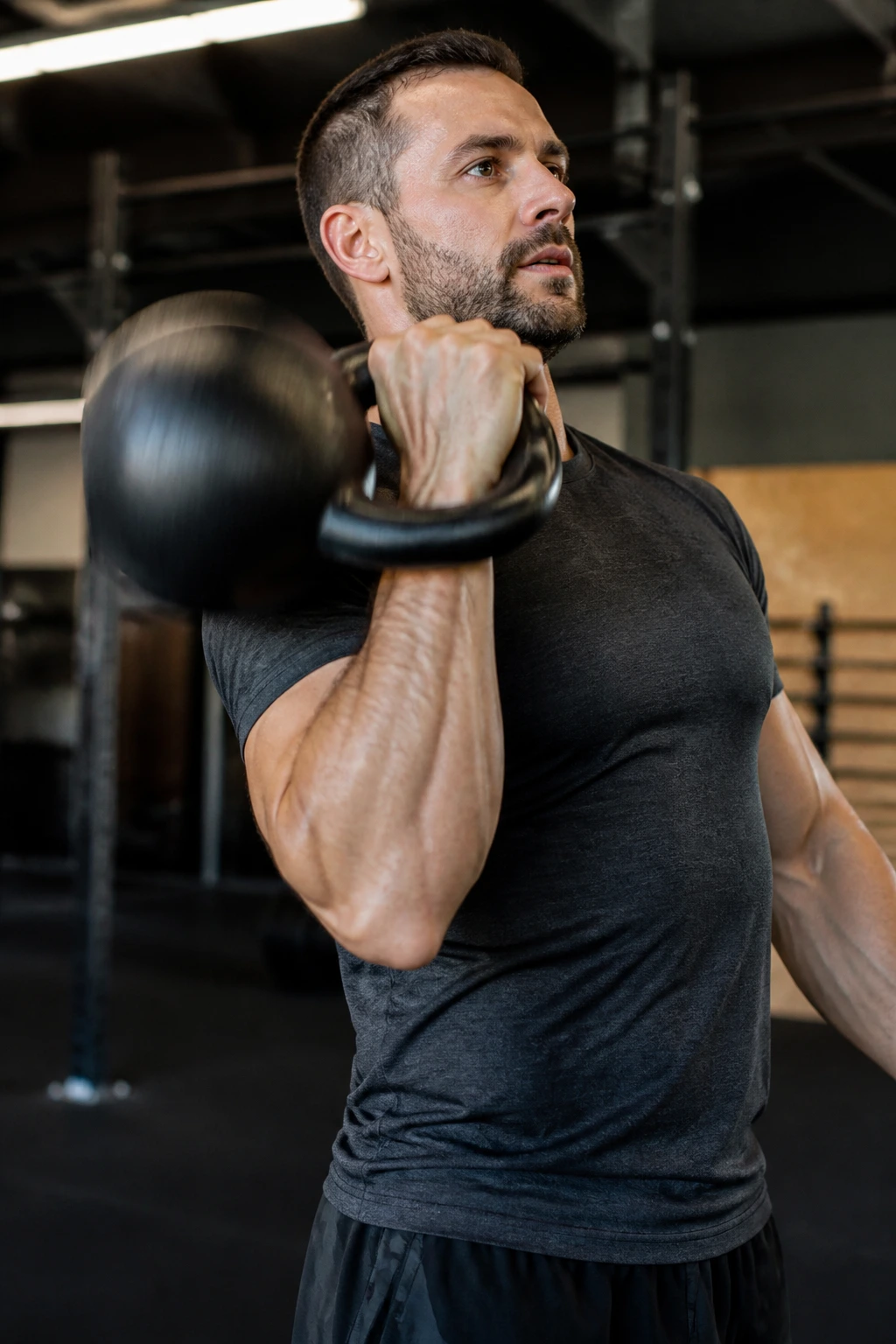 Close-up of kettlebell in long cycle motion with forearm and shoulder visible in a gym.