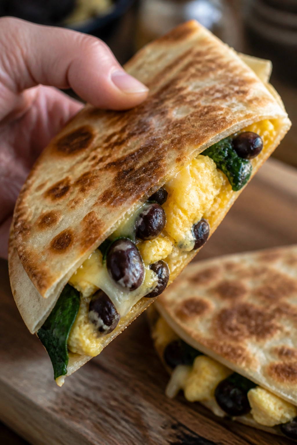 Close-up of folded quesadilla with black beans, eggs and spinach on a wooden board