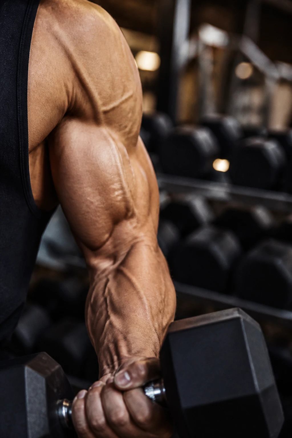 Close-up of a flexed bicep gripping a dumbbell in a gym.