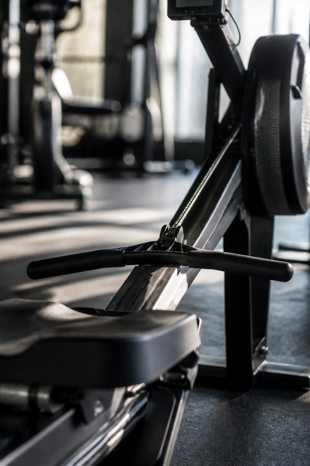 Medium close-up of rowing machine handle and rail in a gym