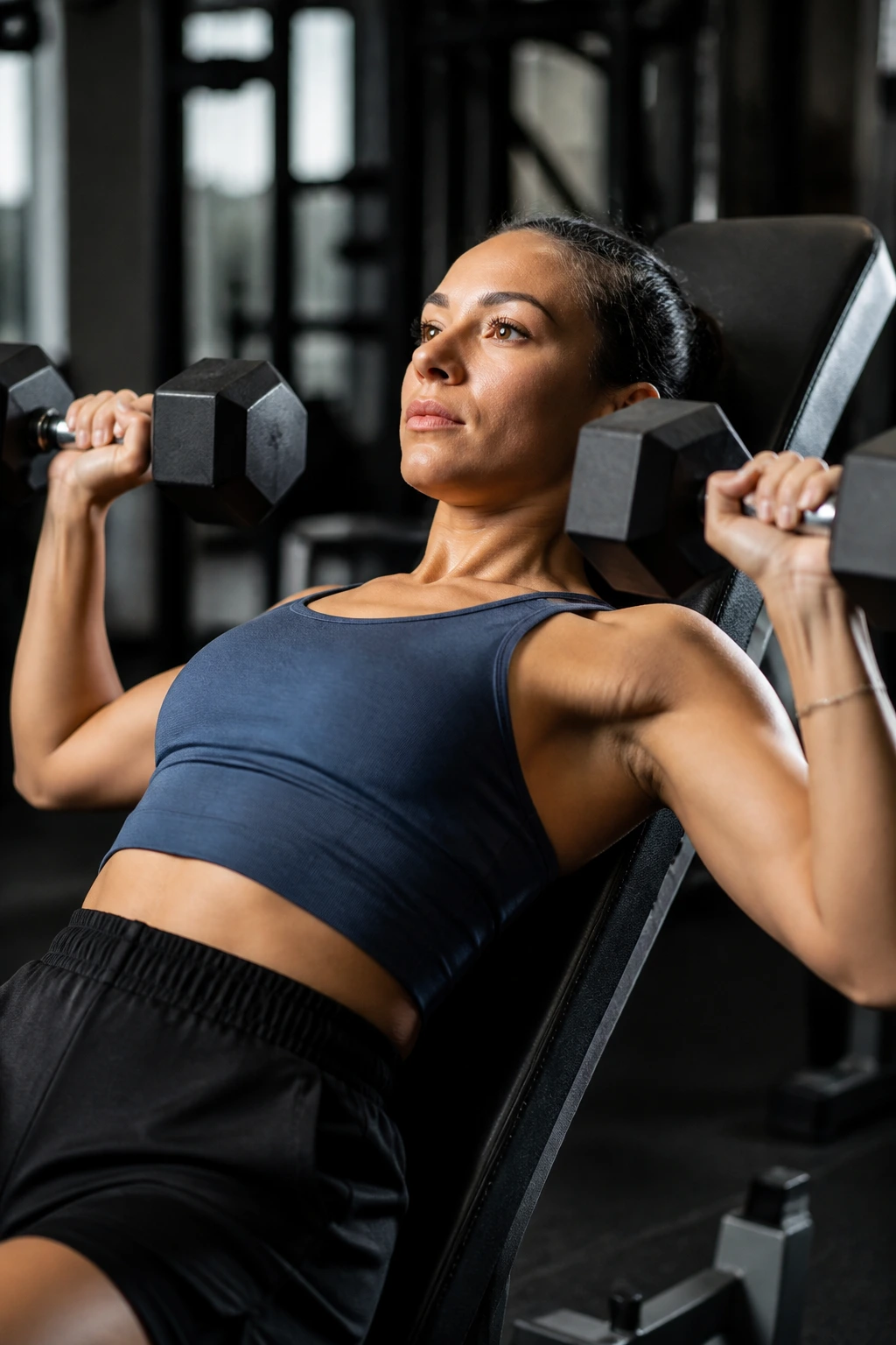 Woman performing incline dumbbell press on incline bench in gym